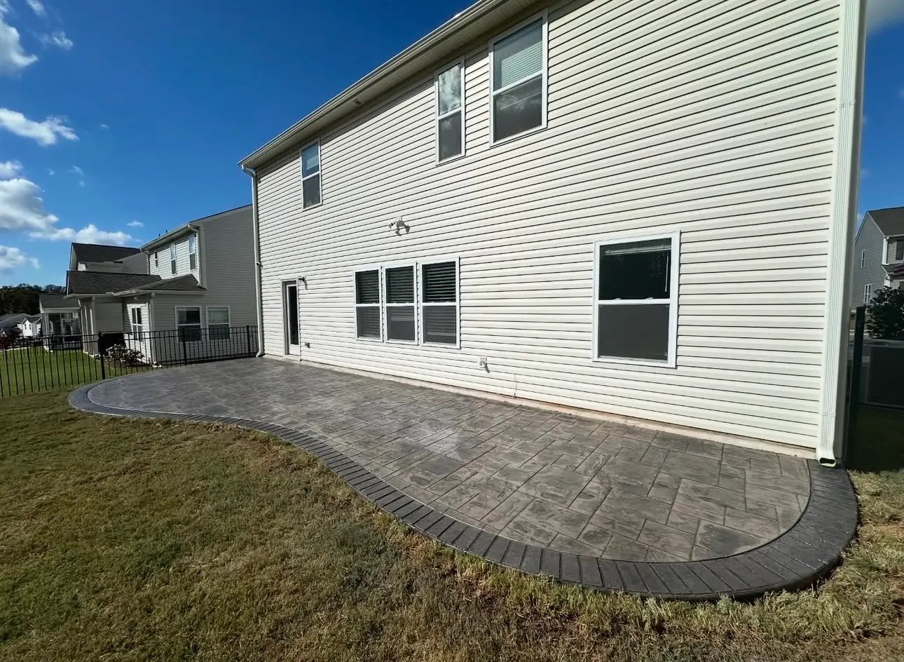 Curved stamped concrete patio with dark border behind a Charlotte home by Rhino Concrete